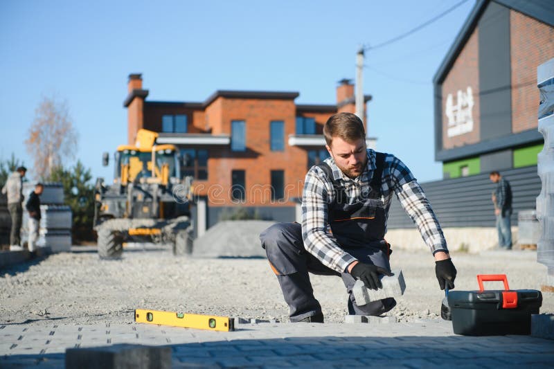 Construction worker installing and laying pavement stones on terrace, road or sidewalk. Worker using stones and rubber stock photography