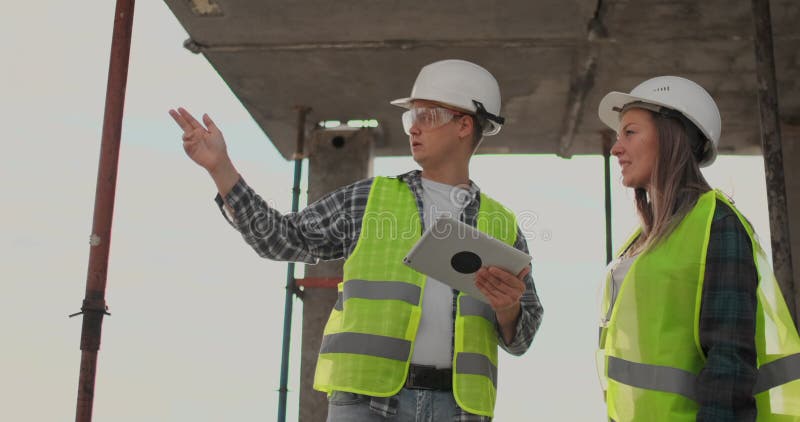 Construction worker man and architect woman in a helmet, discuss the plan of construction of house, tell each other