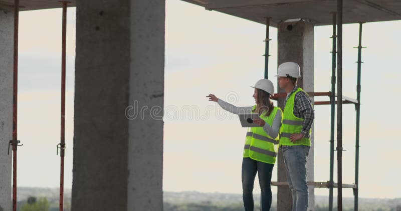 Construction worker man and architect woman in a helmet, discuss the plan of construction of house, tell each other