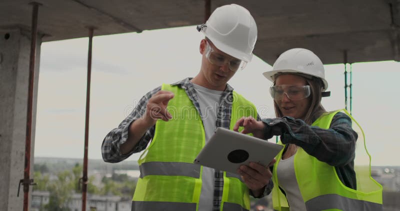 Construction worker man and architect woman in a helmet, discuss the plan of construction of house, tell each other