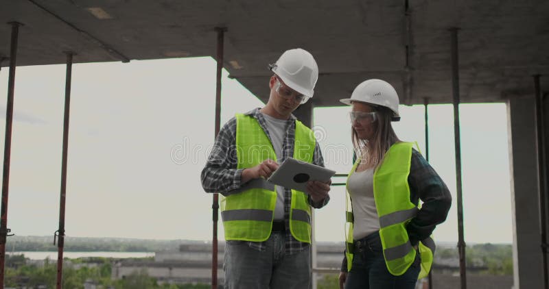 Construction worker man and architect woman in a helmet, discuss the plan of construction of house, tell each other