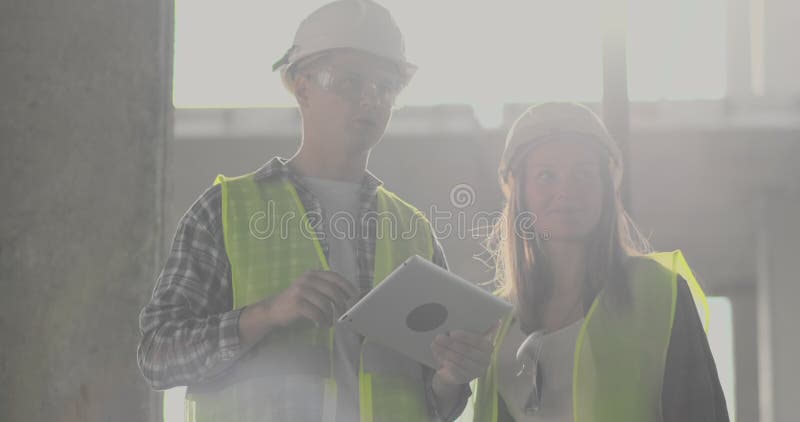 Construction worker man and architect woman in a helmet, discuss the plan of construction of house, tell each other