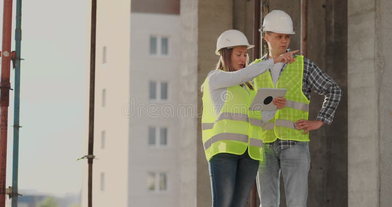 Construction worker man and architect woman in a helmet, discuss the plan of construction of house, tell each other