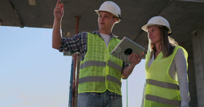 Construction worker man and architect woman in a helmet, discuss the plan of construction of house, tell each other