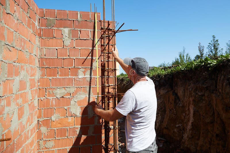 Construction worker measures brick wall at a building site under clear blue sky during daytime stock images