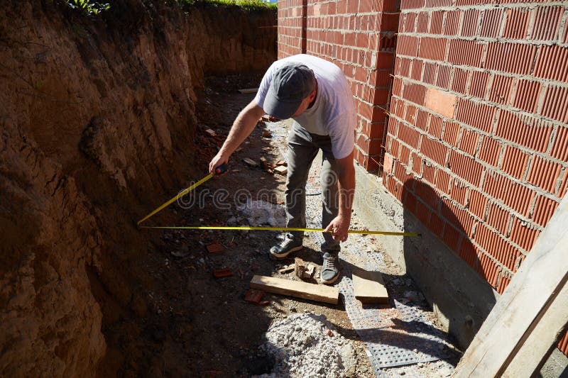 A construction worker measures the width of a pit at a brick wall on a construction site stock photos