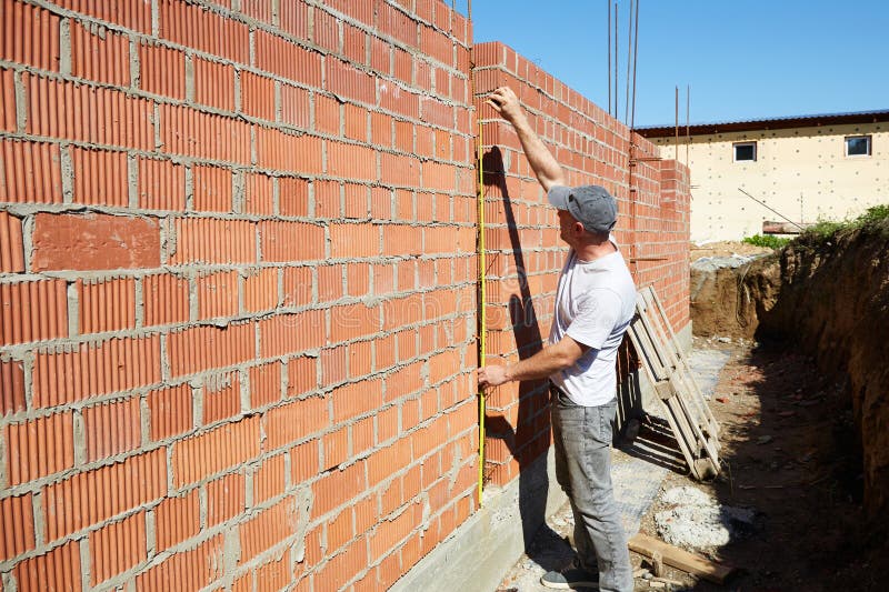 A construction worker is measuring a brick wall at a building site stock photography