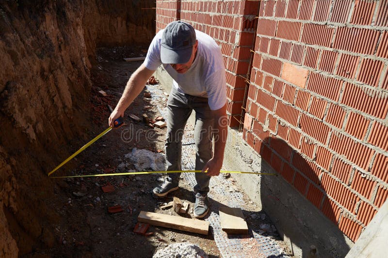 A construction worker is measuring a brick wall at a building site stock photo