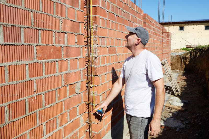 A construction worker is measuring a brick wall at a building site stock photo