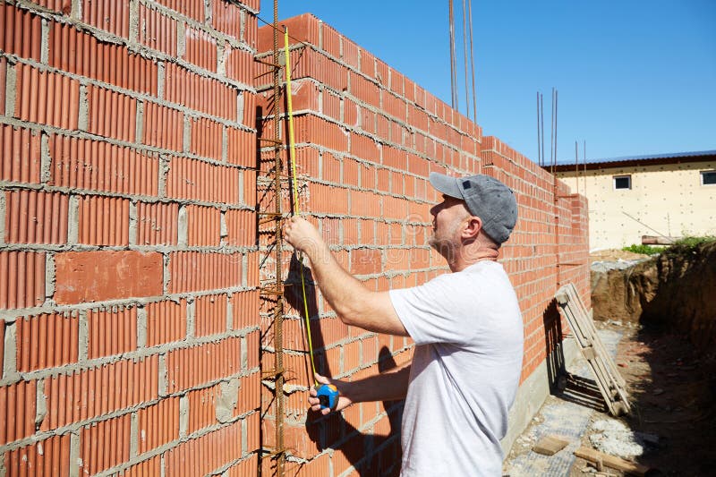 A construction worker is measuring a brick wall at a building site stock images