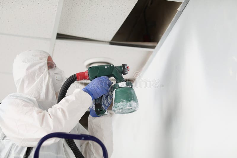 Construction Worker in Protective Suit and Respirator Painting Wall
