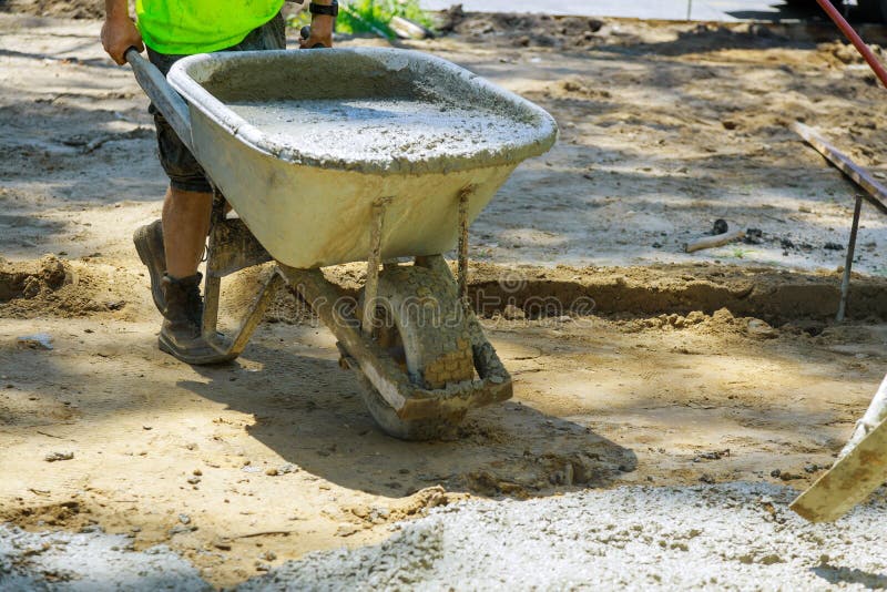 Construction Worker Pushing Wheelbarrow with Concrete at Building Stock