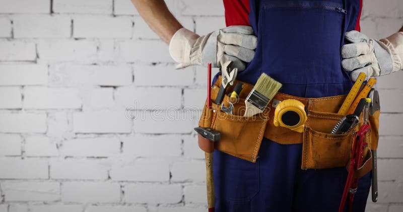 Construction worker with tool belt standing on white brick wall background