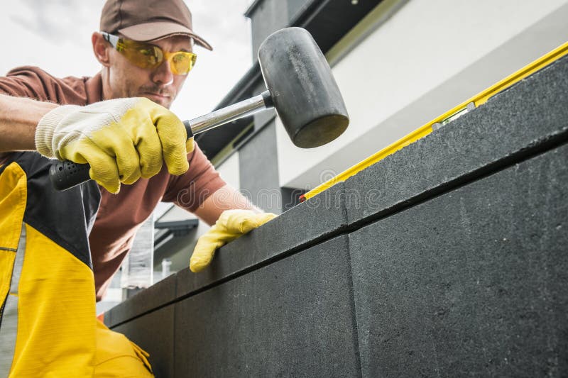 Construction Worker Using a Hammer to Align Blocks While Building a Structure Outdoors stock photos