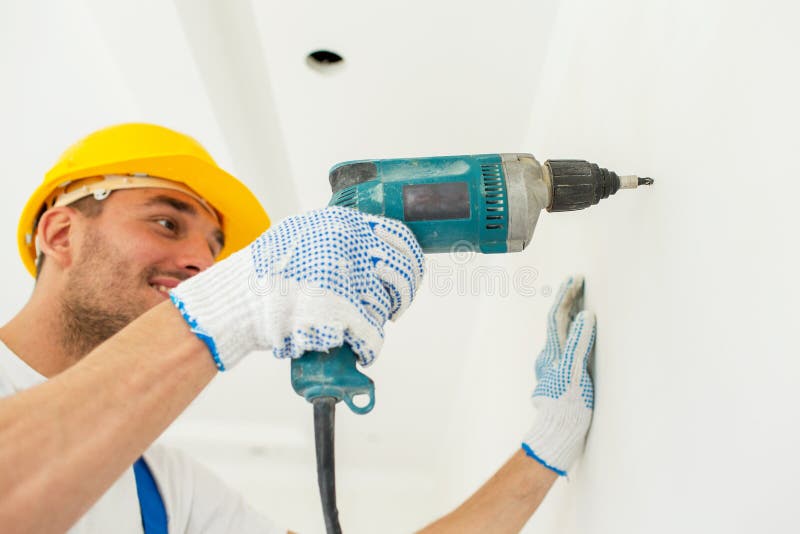 Constructor en el casco de protección con el taladro que perfora la pared imágenes de archivo libres de regalías