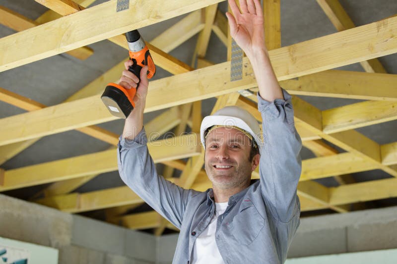 Constructor masculino con perforación inalámbrica en viga de techo fotografía de archivo