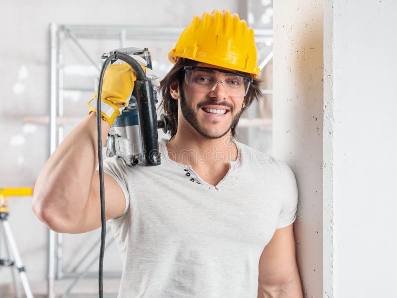 Constructor muscular sosteniendo un taladro sobre un hombro imagen de archivo libre de regalías