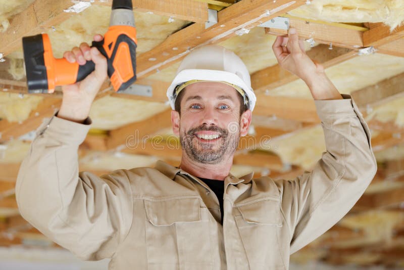 Constructor sonriente en sombrero duro con taladro eléctrico en interiores fotos de archivo