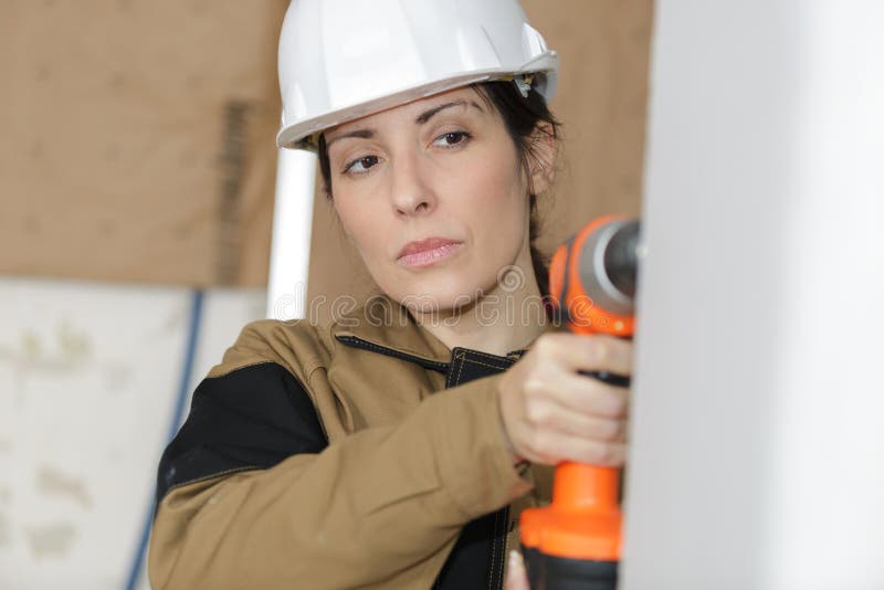Constructora femenina trabajando con taladro eléctrico en paredes fotos de archivo