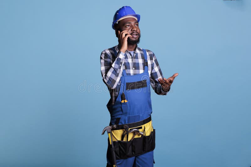Construtor falando sobre smartphone vestindo capa imagem de stock