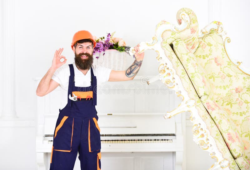 Construtor feliz que relocating o sofá do vintage antes da redecoração Motor de sorriso com barba à moda e bigode que mostra está imagens de stock Construtor feliz que relocating o sofá do vintage antes da redecoração Motor de sorriso com barba à moda e bigode que mostra está imagens de stock