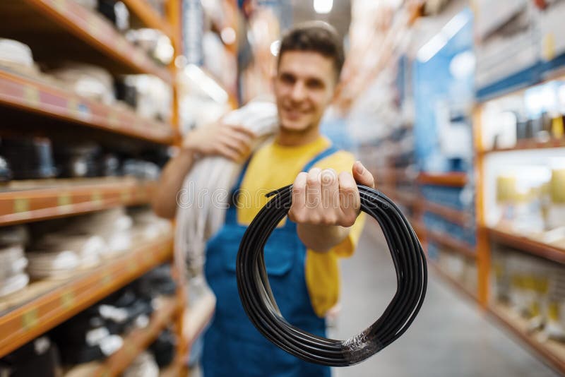 Male builder with coil of wires in hardware store. Constructor in uniform look at the goods in diy shop. Male builder with coil of wires in hardware store. Constructor in uniform look at the goods in diy shop