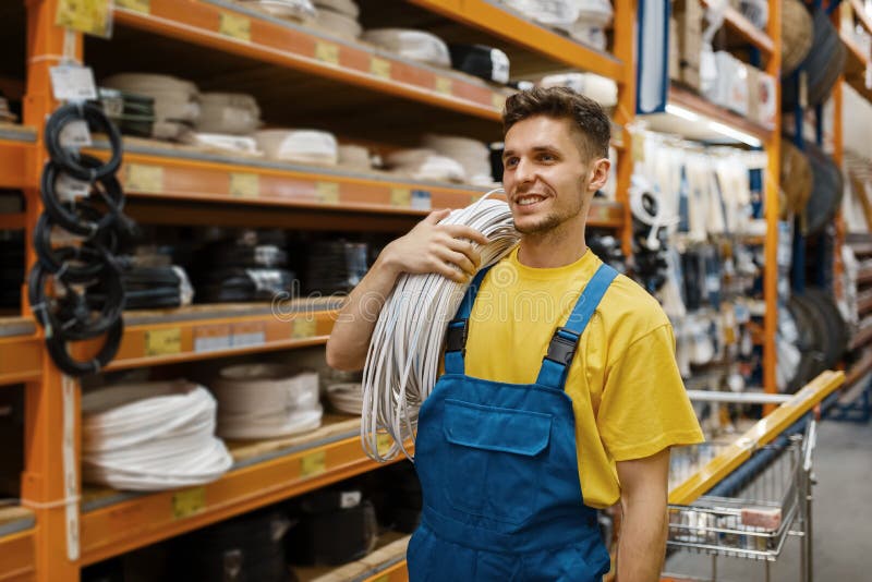 Male builder with coil of wires in hardware store. Constructor in uniform look at the goods in diy shop. Male builder with coil of wires in hardware store. Constructor in uniform look at the goods in diy shop