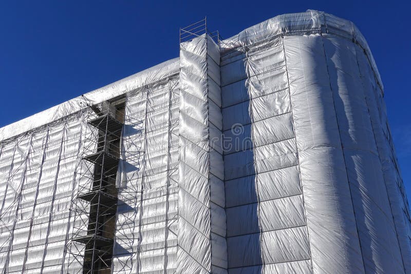 House building, construction, restoration or maintenance site with scaffolding and protective covering of gray tarpaulin. House building, construction, restoration or maintenance site with scaffolding and protective covering of gray tarpaulin