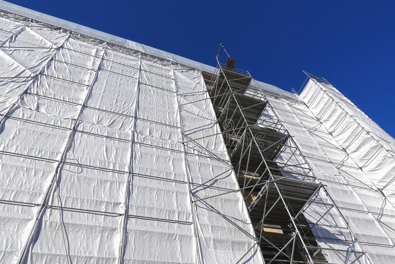 House building, construction, restoration or maintenance site with scaffolding and protective covering of gray tarpaulin. House building, construction, restoration or maintenance site with scaffolding and protective covering of gray tarpaulin.