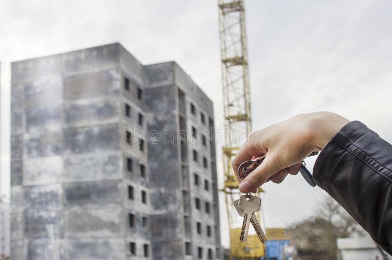 A construção de uma casa residencial, uma mão fêmea guarda as chaves ao apartamento, construindo foto de stock A construção de uma casa residencial, uma mão fêmea guarda as chaves ao apartamento, construindo foto de stock