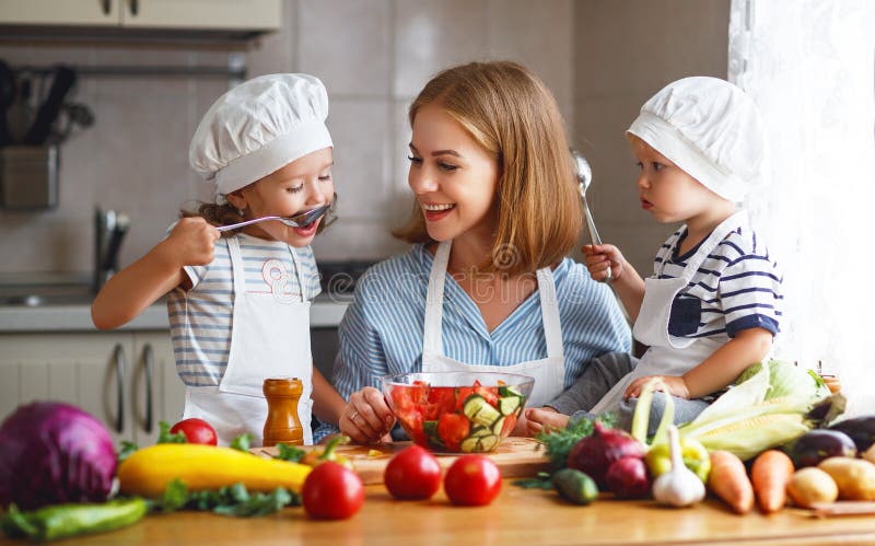 Consumición sana La madre y los niños felices de la familia prepara la ensalada vegetal