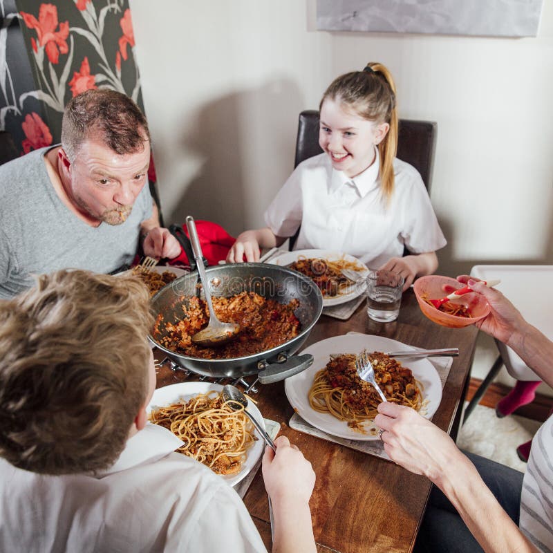 British family enjoying a spagetti bolognese together at home. The children are laughing as their father has spagetti hanging out his mouth. British family enjoying a spagetti bolognese together at home. The children are laughing as their father has spagetti hanging out his mouth.