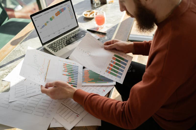 Contador masculino que trabaja con documentos usando un informe de lectura de laptop con gráficos que preparan datos contables foto de archivo libre de regalías