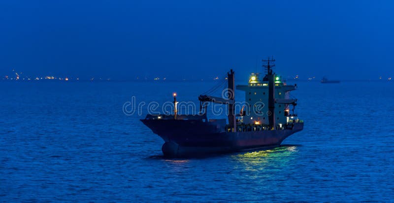 Container cargo ship with navigation lights anchored in outer anchorage of Singapore at night