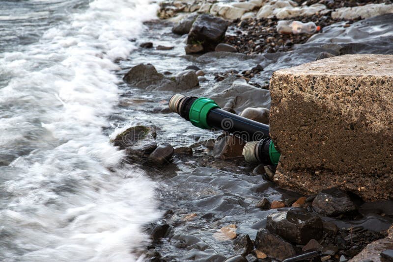 Contaminated water, sewage waste is drained through pipe into sea on an unequipped beach. Pollution of environment, ecological cat royalty free stock images