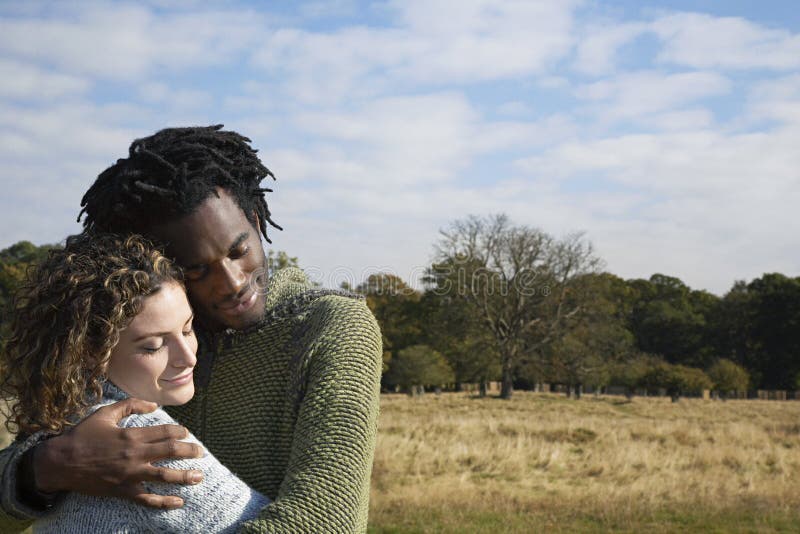 Contented young multiethnic couple embracing in field. Contented young multiethnic couple embracing in field