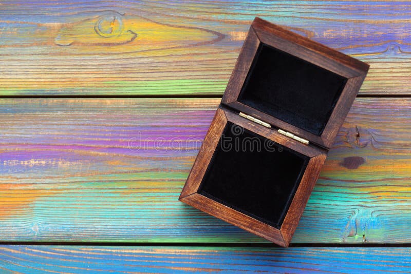 Contenitore di gioielli di legno aperto con l'interno nero del velluto su un fondo di legno colorato luminoso fotografie stock