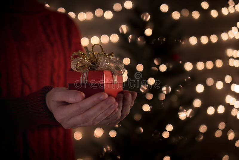 Contenitore di regalo rosso di tenuta femminile di Natale sul fondo delle luci del bokeh fotografia stock Contenitore di regalo rosso di tenuta femminile di Natale sul fondo delle luci del bokeh fotografia stock