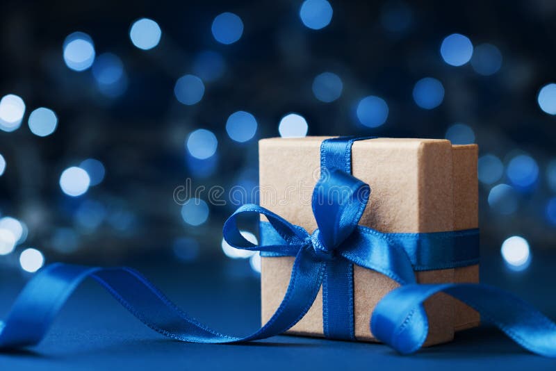 Contenitore o presente di regalo della festa con il nastro dell'arco contro il fondo blu del bokeh Cartolina d'auguri magica di n