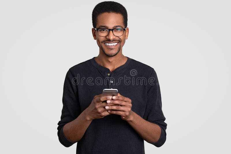 Content Smiling Male With Curly Hair Dark Skin White Teeth Being In High Spirit Carries Mobile Phone Enjoys Online Stock Photo Image Of Alone Internet 132562394