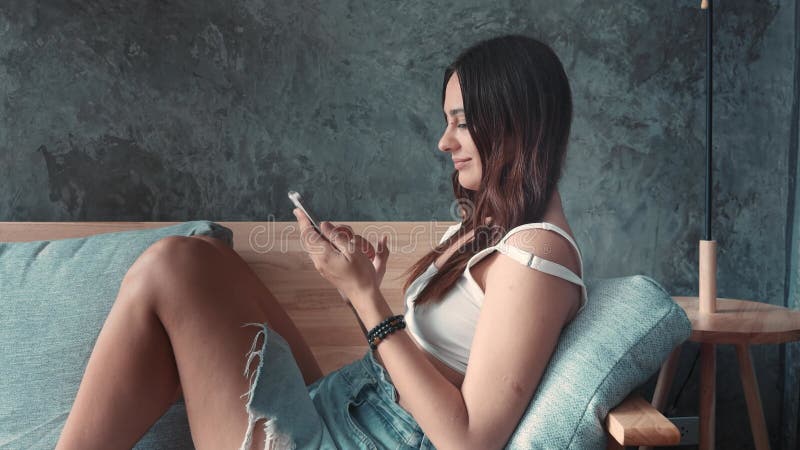 Contentedly sitting on sofa woman rests engaged with phone. Woman rests embodying essence of home relaxation In