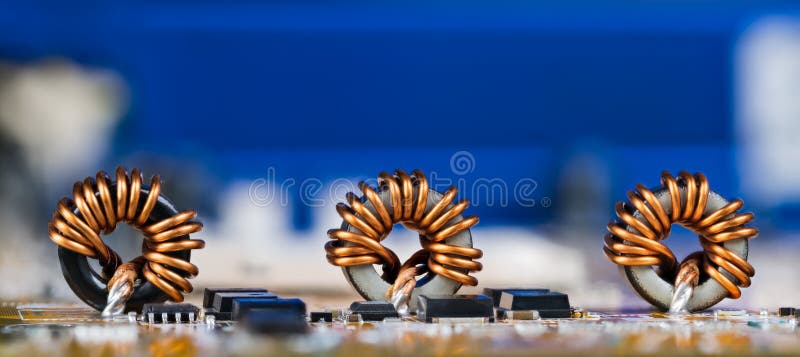 Electronic components as coils or transistors on circuit board detail. Copy space on a blue blurry device. Electronic components as coils or transistors on circuit board detail. Copy space on a blue blurry device