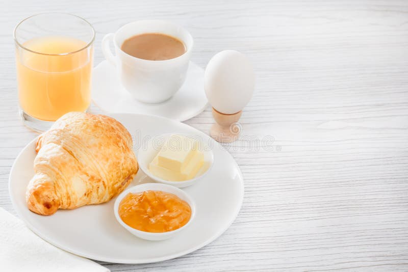 Continentaal ontbijt met een croissant, gekookt ei Koffie of thee met melk, een glas sap, broodjes, boter, jam royalty-vrije stock afbeelding Continentaal ontbijt met een croissant, gekookt ei Koffie of thee met melk, een glas sap, broodjes, boter, jam royalty-vrije stock afbeelding