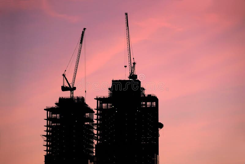 Contours of tower cranes above the high constructing tower buildings against evening sky in the red sunset