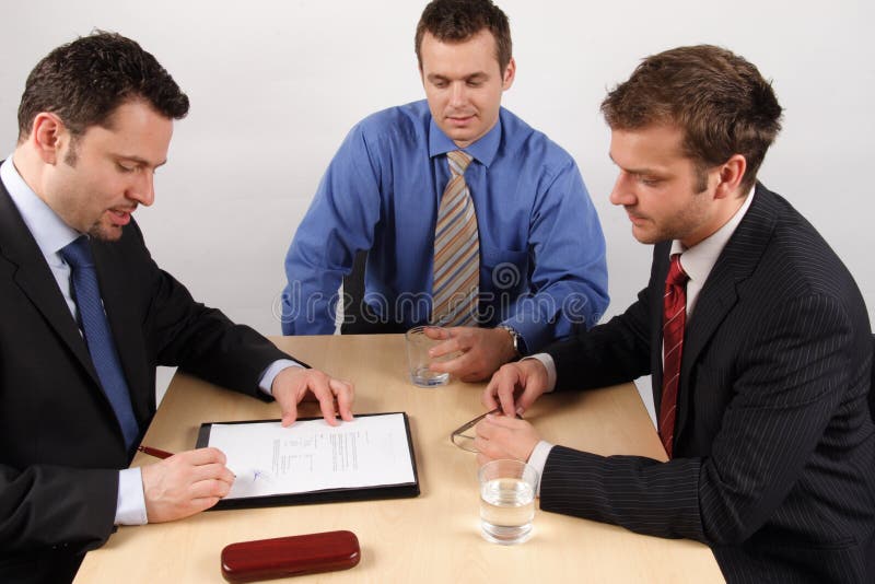 Three businessmen sitting at a table negotiating and signing a contract. Negotiating table stock images, royalty-free photos and pictures