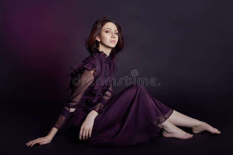 Contrast fashion Armenian woman portrait with big blue eyes sit on a dark background in a purple dress. Lovely gorgeous girl