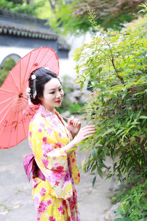 Control japonés asiático tradicional de la novia de la mujer un paraguas rojo que sonríe en un jardín imagenes de archivo Control japonés asiático tradicional de la novia de la mujer un paraguas rojo que sonríe en un jardín imagenes de archivo