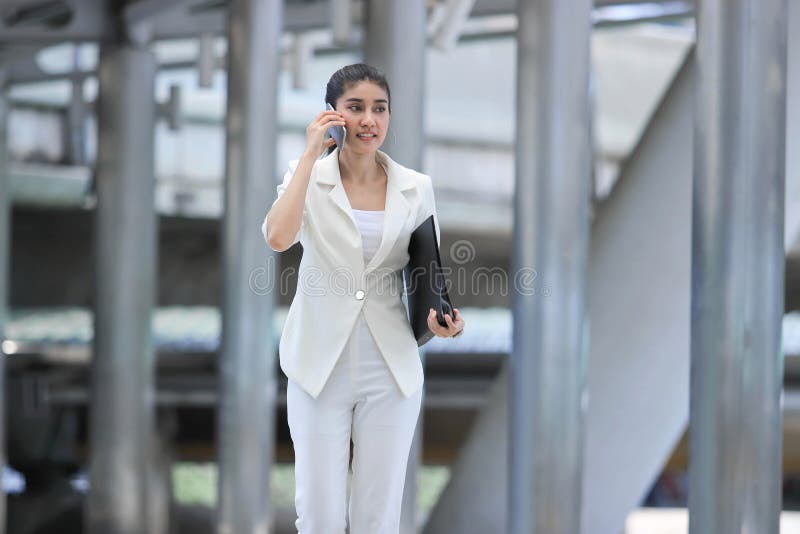 Conversa asiática nova atrativa da mulher de negócio no telefone durante o passeio ao escritório imagens de stock Conversa asiática nova atrativa da mulher de negócio no telefone durante o passeio ao escritório imagens de stock