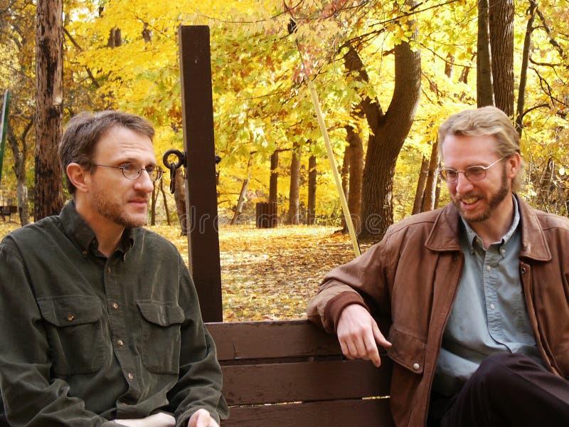 Two men on park bench, one smiling, one with distressed look. Two men on park bench, one smiling, one with distressed look