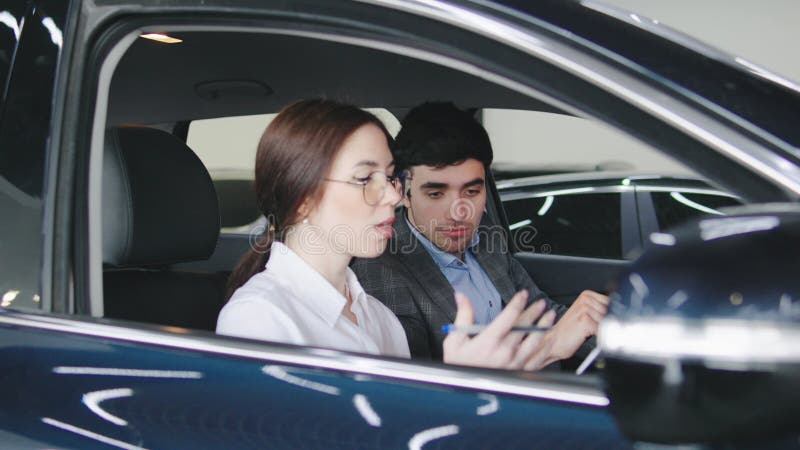 Conversazione di concessionari di auto tra un giovane e una donna che discutono di caratteristiche e opzioni mentre si siede all'i video d archivio